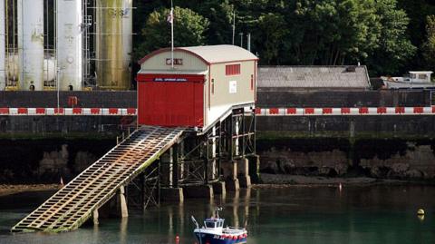 The boathouse which looks worn out, there is a red large door and a rusted slipway into the quay.