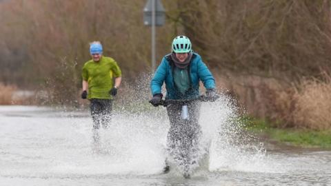 People running and cycling on a flooded road in Leicestershire