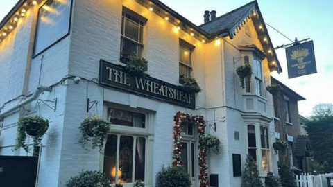 The outside of the Wheatsheaf pub - a white brick building with a pitched black roof. There are Christmas lights lining the roof.