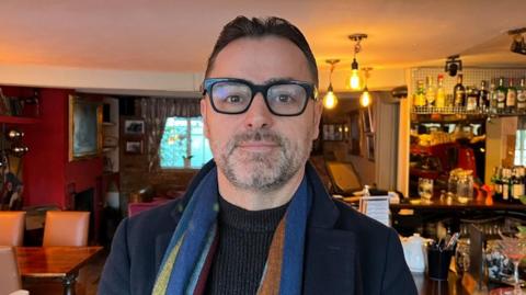 Cimi Kazazi stood inside his pub looking at the camera for a photo.