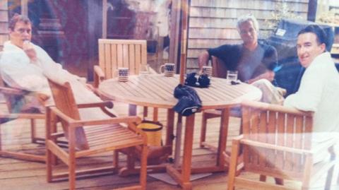 An image of Andrew Mountbatten-Windsor, Jeffrey Epstein and Peter Mandelson sat around a wooden table. 