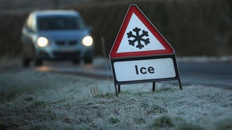 A road sign with a snowflake icon. There is a car driving on the road.