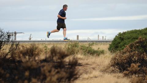 A jogger passes charred ground and foliage caused by Wildfires in Halkyn, Britain, 27 July 2026.