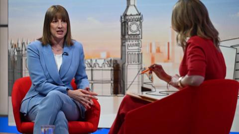 Rachel Reeves sits on a red armchair and wears a blue suit and sits opposite Laura Kuenssberg who is seated on a red armchair in a red dress, while appearing on the BBC 1 current affairs programme, Sunday with Laura Kuenssberg.