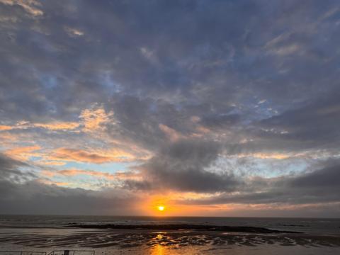 Grey sky over the coast with a setting sun in the distance 