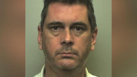 A police mugshot of Mark Robert Witchell. He is wearing a light-coloured top and is looking directly at the camera.
