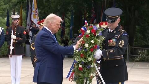 Donald Trump puts his hand on a wreath
