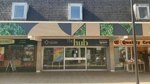 The Hub shop front photographed on a sunny day. The premises' front shows a class entrance with a dark grey sign that reads "The Hub" in white and green writing. 