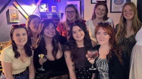 A group of young women pose together with their drinks in a pub and all smile.