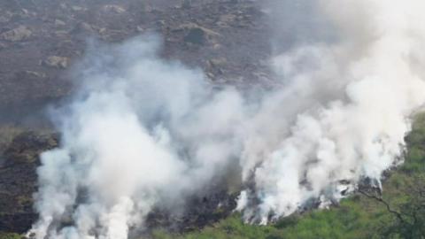 Smoke can be seen billowing off moorlands after a fire quickly spread in the area. Patches of burnt grass be seen on the moorlands. 