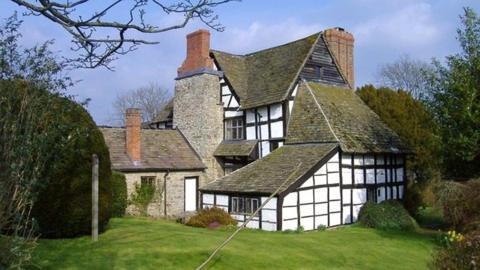 A black and white farmhouse with a green lawn and bushes, with a blue sky overhead