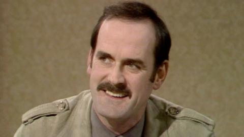 John Cleese smiling, whilst being interviewed by Mervyn Bragg.