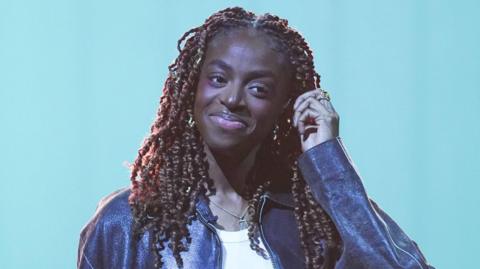 Cat Burns pictured smiling and wearing a leather jacket during filming for the Graham Norton Show in December