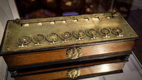 Close-up of La Pascaline, a brass wooden box accented with a line of small metallic wheels on top.