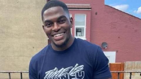 Chris Kaba in a casual photo, wearing a T-shirt and smiling at the camera