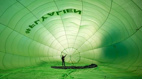 A man is standing in a giant green balloon as it inflates 