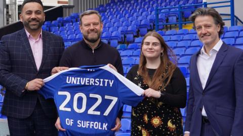 Four people showing off a replica Ipswich Town football shirt at Portman Roadd