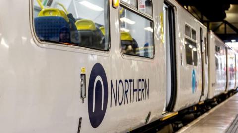 Close up of a white Northern rail train with its logo in blue on carriage at a railway station platform 