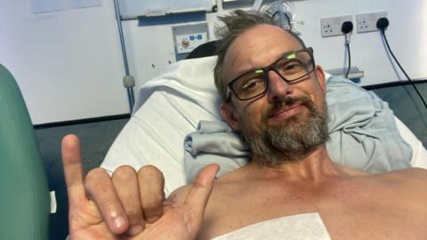 Stuart Humphrey - a man with glasses and a brown and grey beard. He is lying in a hospital bed.