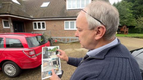 Homeowner Steve Dally stands in front of his new extension holding pictures of the 1960s garage that was there before.