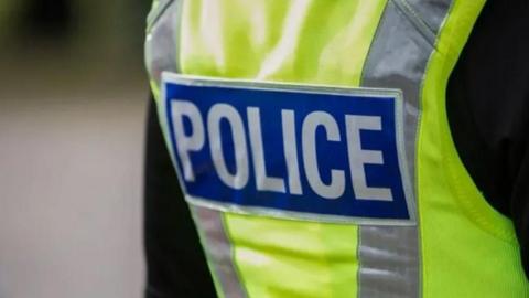 The back of a uniformed police officer, wearing a high-visibility jacket, with the word "police" printed.