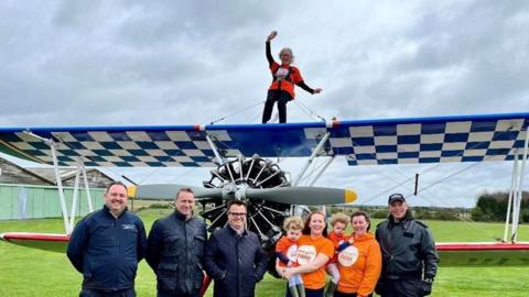 Josie Howley on the wings of a Boeing Stearman bi-plane with a group of people beneath her