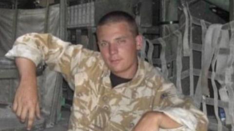 A soldier in the back of a military vehicle. He is in uniform.