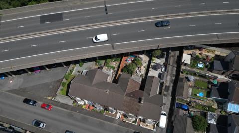 A motorway with cars and vans on it running over the top of a row of terraced houses, seen from overhead 