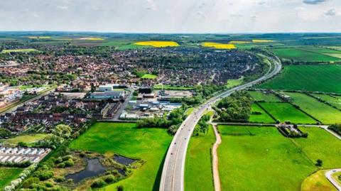 An aerial view of Barton-upon-Humber showing the A15 dual carriageway heading south, the town can be seen on the left of the photo and green fields to the right and in the background.