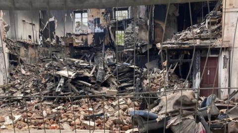 Burned rubble and bricks sit alongside a red door which says '2A'