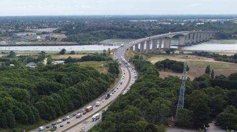 A drone image of the A14 looking toward the Orwell Bridge. The bridge can be seen in the distance. Queues of traffic can be seen on the carriageway.