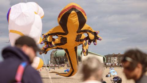 A large yellow salamander kite with purple patches on the tips of its feet. Blurred people can be seen in the foreground.