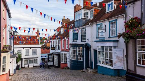 Row of shops in a cobbled stone street of grade II listed buildings.