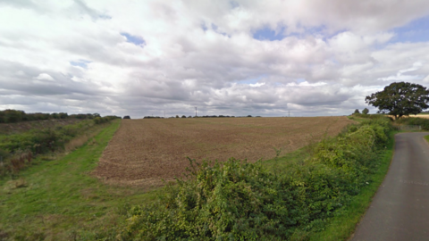 A Google Maps picture of arable land, surrounded by hedgerows, and a road on the right. 