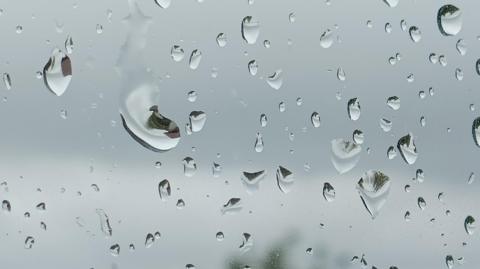 Raindrops on a window, with a grey sky in the background