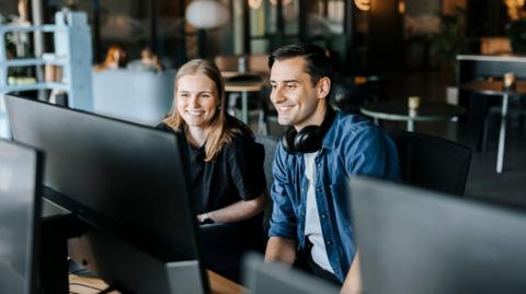 Happy male and female entrepreneurs watching computer screen sitting in tech startup office - stock photo