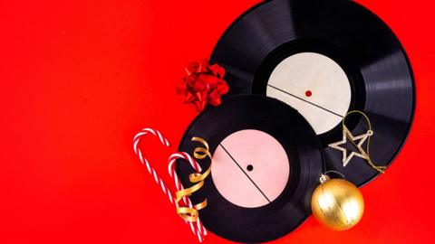 Vintage retro vinyl records for gramophone player, with Christmas decorations and gift boxes on red background. 
