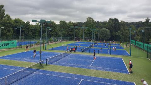 Four new tennis courts, which are blue and green, with people playing on them 