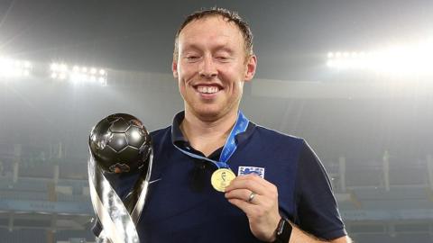 Steve Cooper holds the silver Under-17 trophy in his right hand and raises his gold medal in his left hand