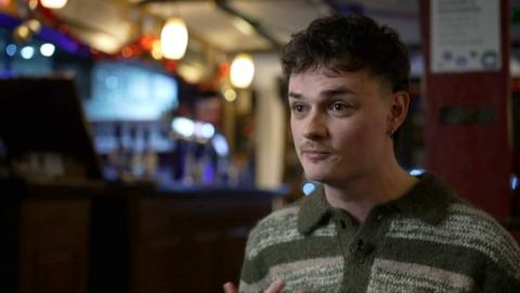Film director Stuart Armstrong, wearing a jumper with horizontal green stripes. A bar is visible in the background.