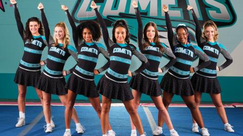 Cheerleaders in uniform in a row with their right arms in the air