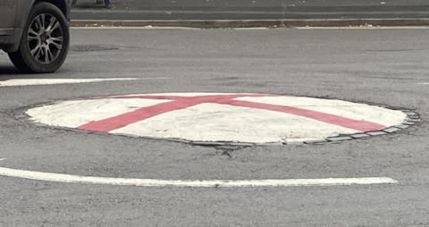 A mini roundabout which has been painted with the flag of St George, in Bromsgrove. A car can be seen being driven around it in the top left of the picture.