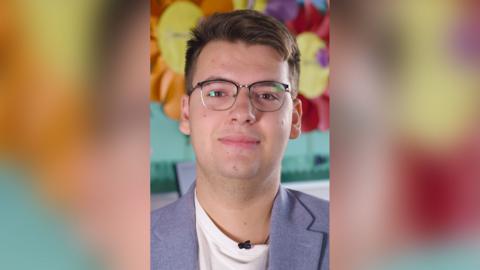 Nazarii Lialiuk in a white t-shirt and light blue blazer. He is wearing glasses with a half black rim.