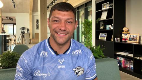Ryan Hall, who has short dark hair and dark eyes. He is smiling in the photo and wearing a blue Leeds Rhinos jersey.
