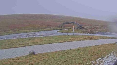 A view of the Mountain Road, there is some snow on the grass, you can see a bridge to cross the route.