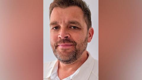 A head and shoulders picture of a man with a beard 