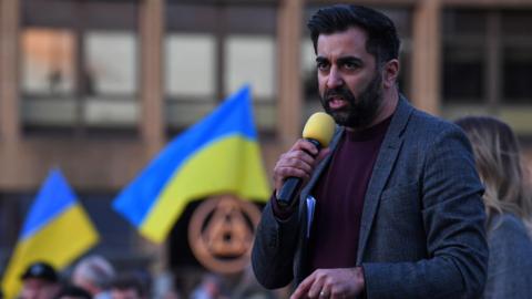 Humza Yousaf speaking to a crowd waving Ukranian flags in 2023 on the first anniversary of Russia's invasion of Ukraine