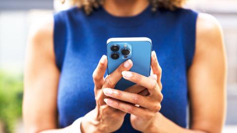 Close up of a woman wearing a sleeveless blue top, using a blue smart phone.