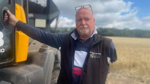 Farmer James poses for the camera, holding on to his tractor with his right arm, his left missing