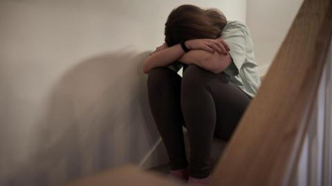 A woman sits on a staircase with her head resting on her crossed arms.